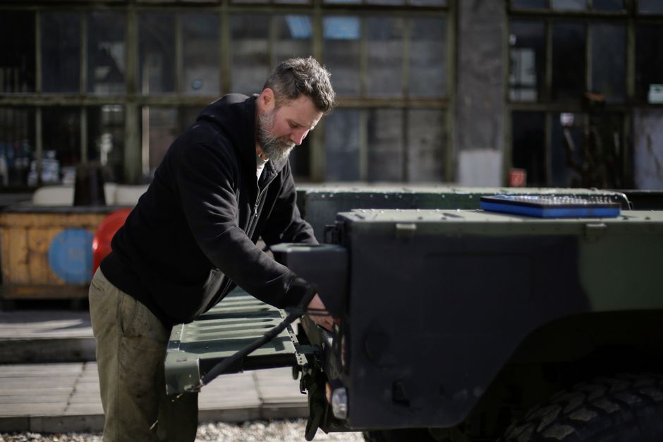 Side view of serious adult bearded mechanic in workwear standing on street near garage and fixing door of trunk